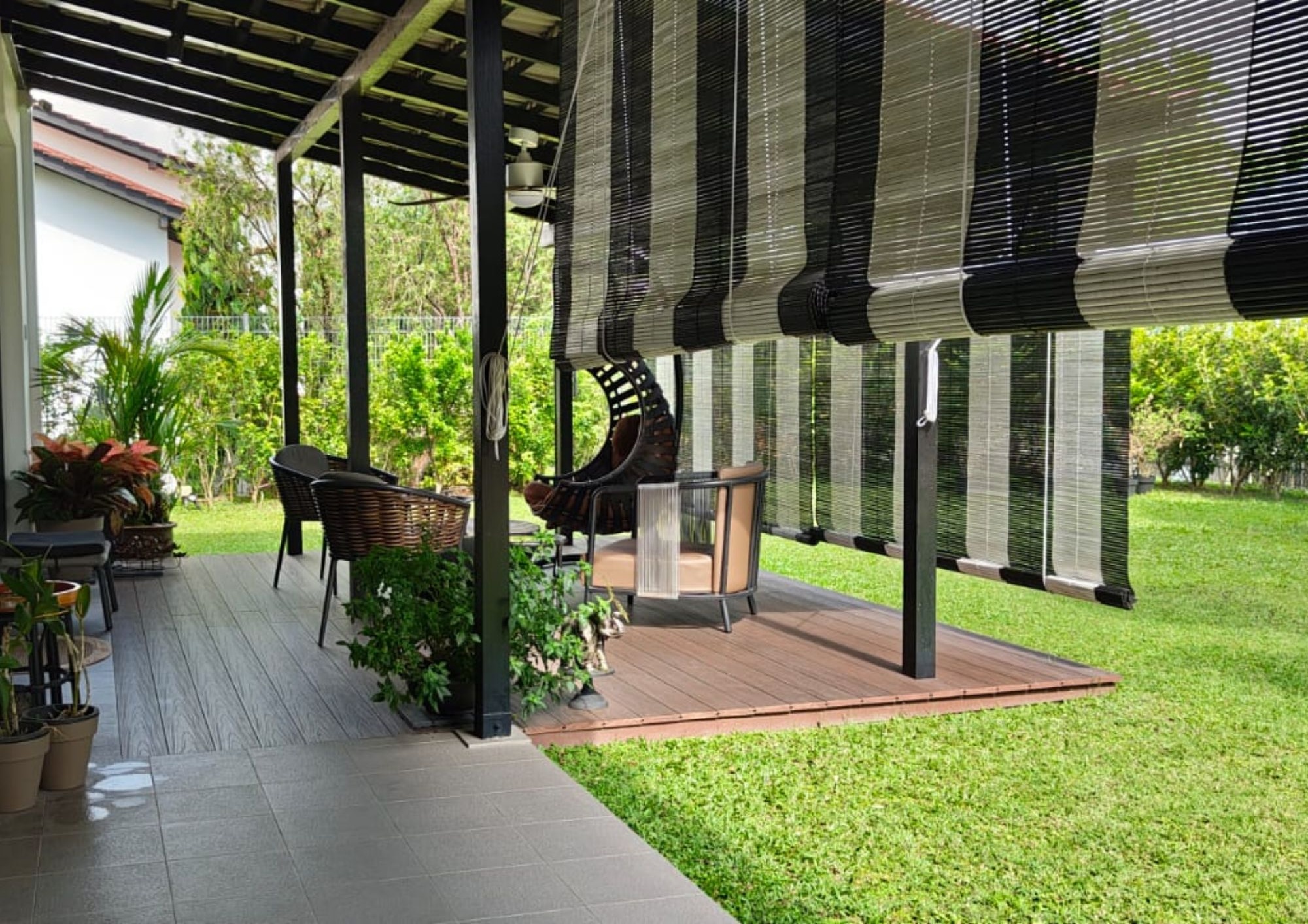 Garden patio with timber deck, black steel pergola, roller blinds and lush tropical lawn