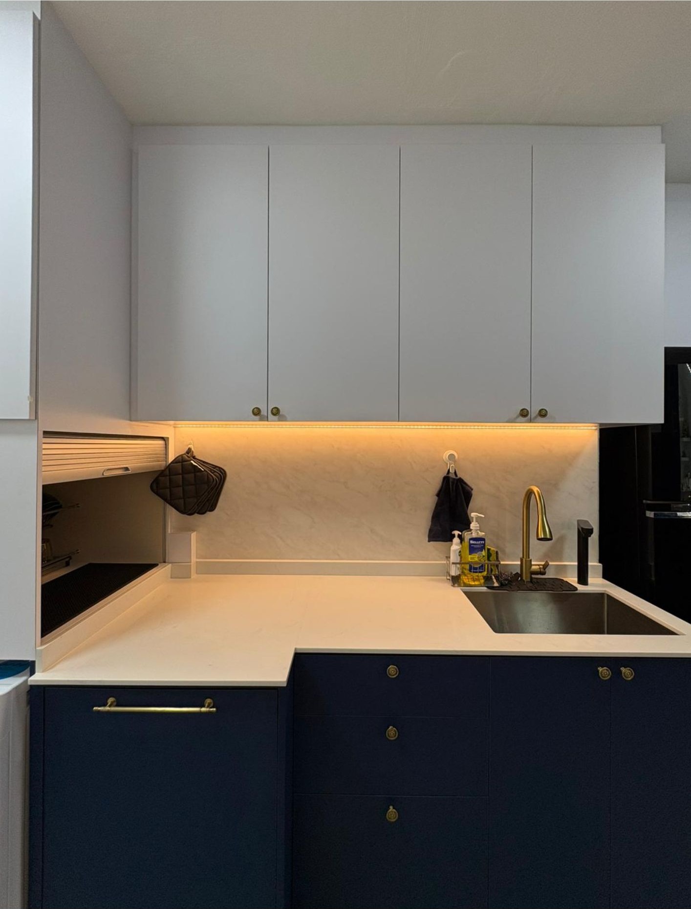 Kitchen with navy blue lower cabinets, brass knobs, white uppers, marble splashback and brass tap