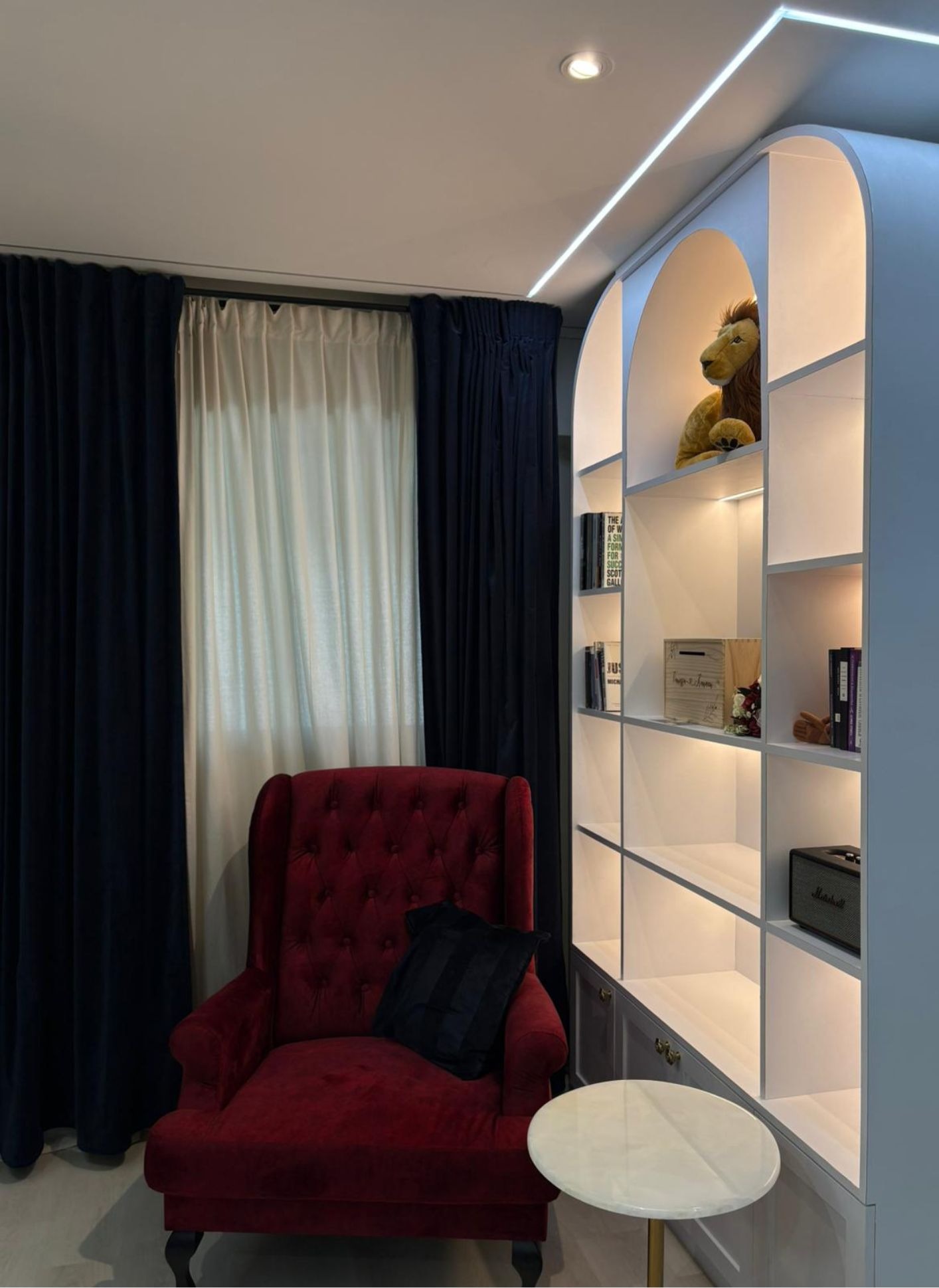 Modern luxe living room with red velvet armchair, navy curtains and arched display shelf in Potong Pasir HDB