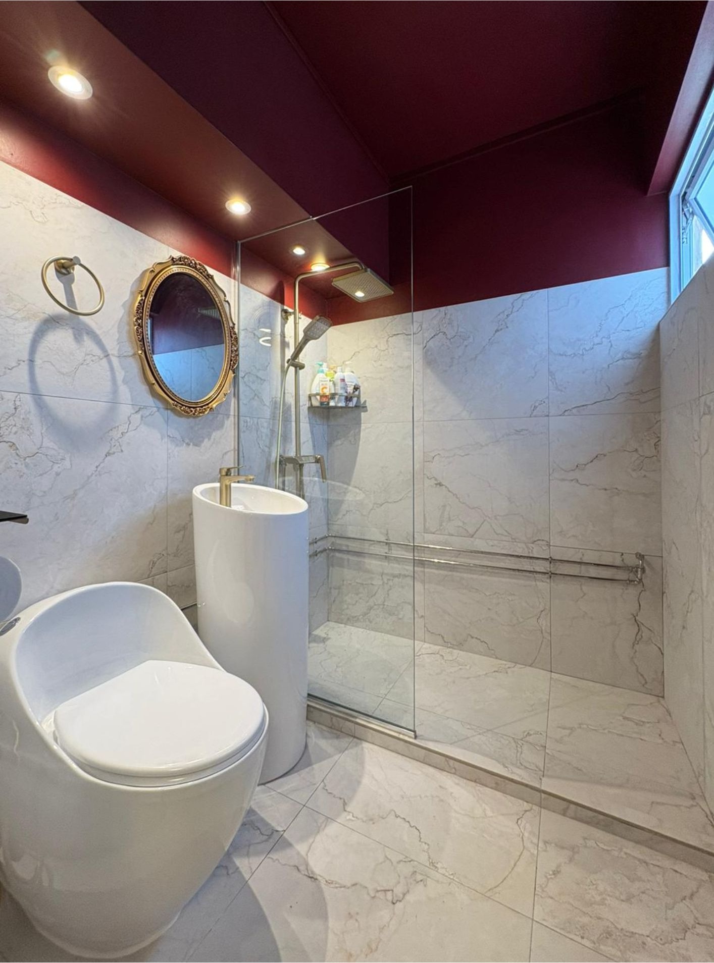 Master bathroom with white marble tiles, burgundy ceiling, gold ornate mirror and glass shower