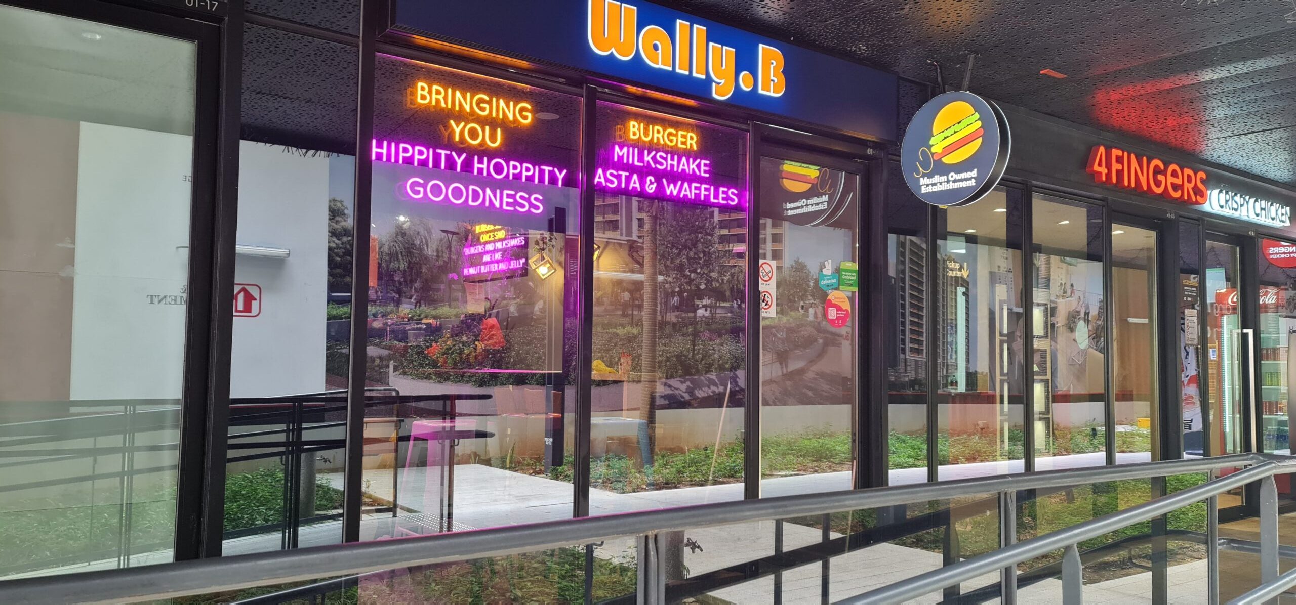 Wally B storefront at LeQuest with neon logo and menu signage next to 4FINGERS