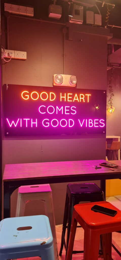 Neon sign 'Good Heart Comes With Good Vibes' with colourful metal bar stools and high table