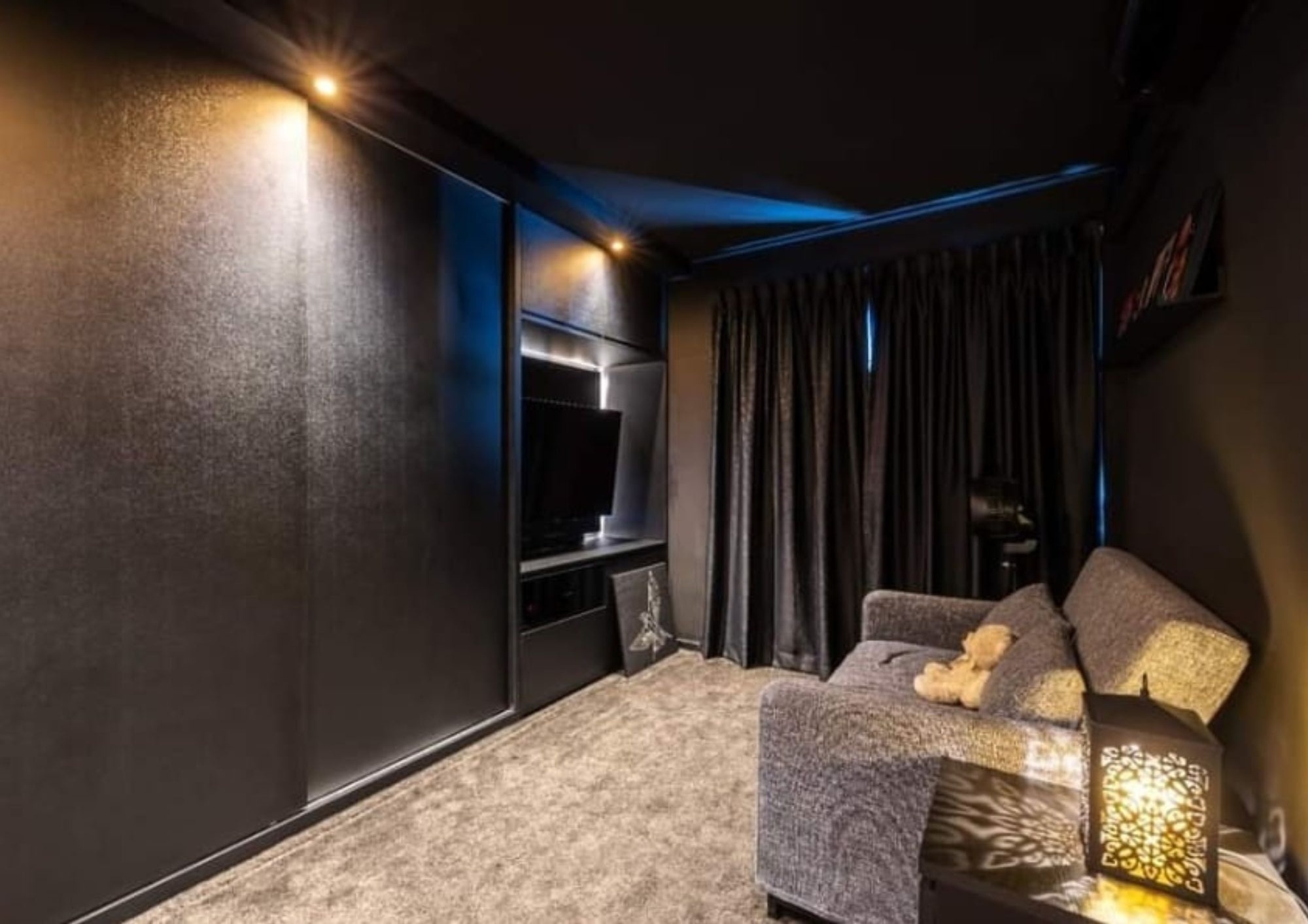 Home theatre room with dark walls, dark curtains, grey sofa, Moroccan lamp and blue LED accent lighting